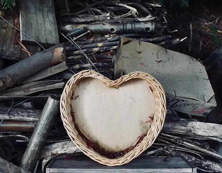 A heart-shaped basket sitting on top of a pile of spare pieces of wood and tree branches