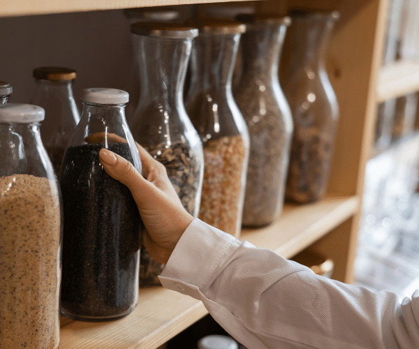 Hand reaching for glass bottle full of brown rice, trade concept without plastic packaging